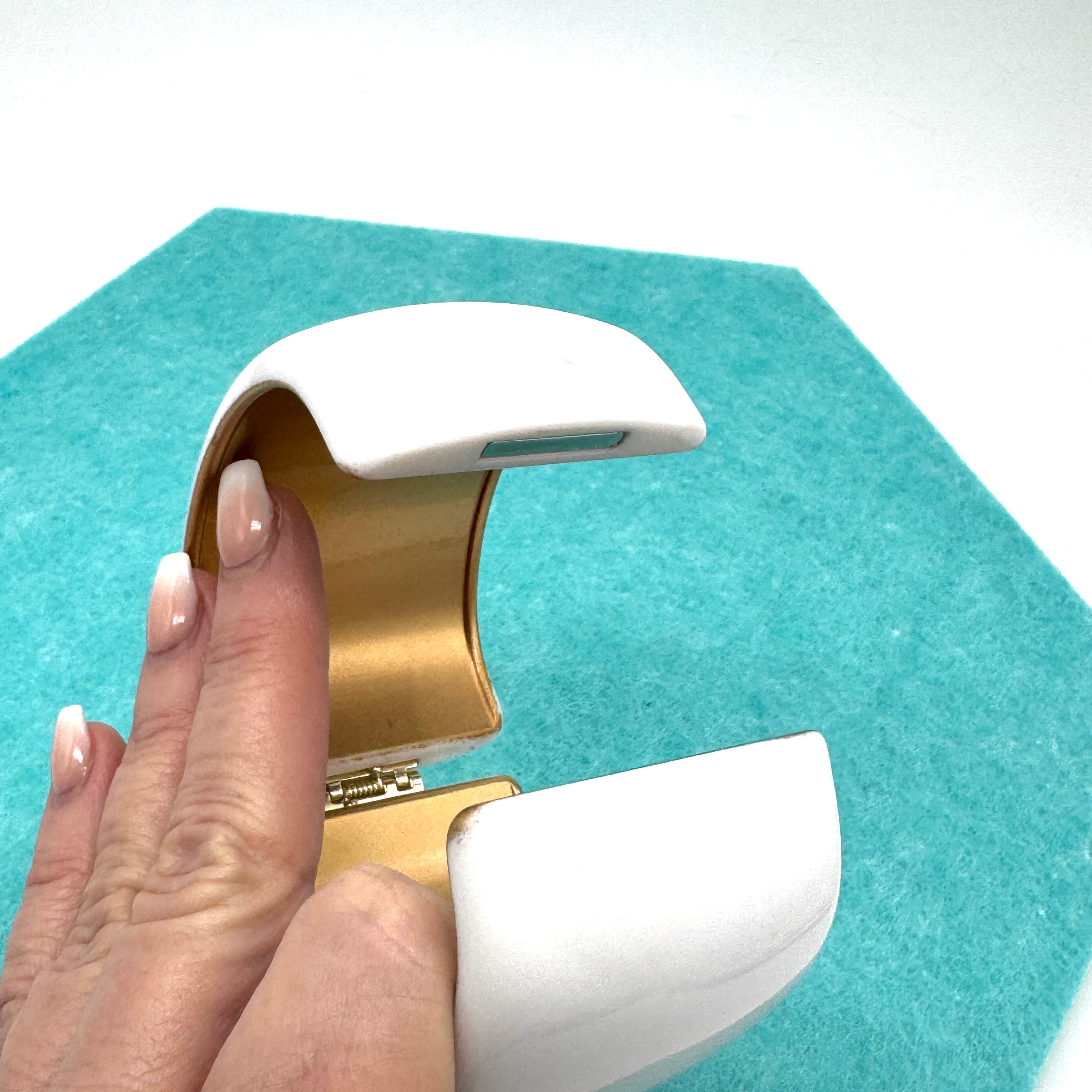 white lucite clamper cuff bracelet held open on a blue background