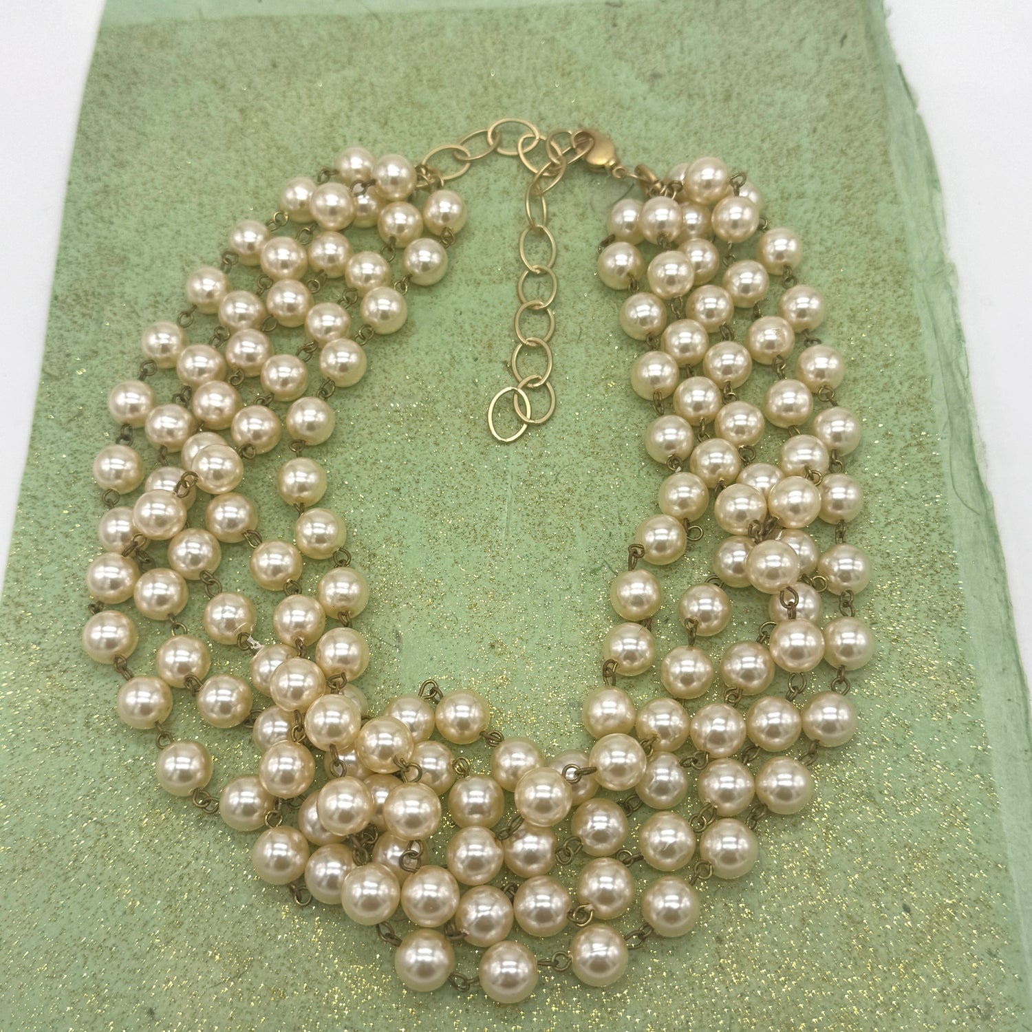Multiple strands of pearls on a green textured surface