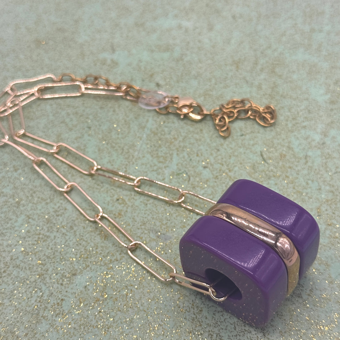 Chain necklace with a purple pendant on a textured surface