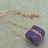 Chain necklace with a purple pendant on a textured surface