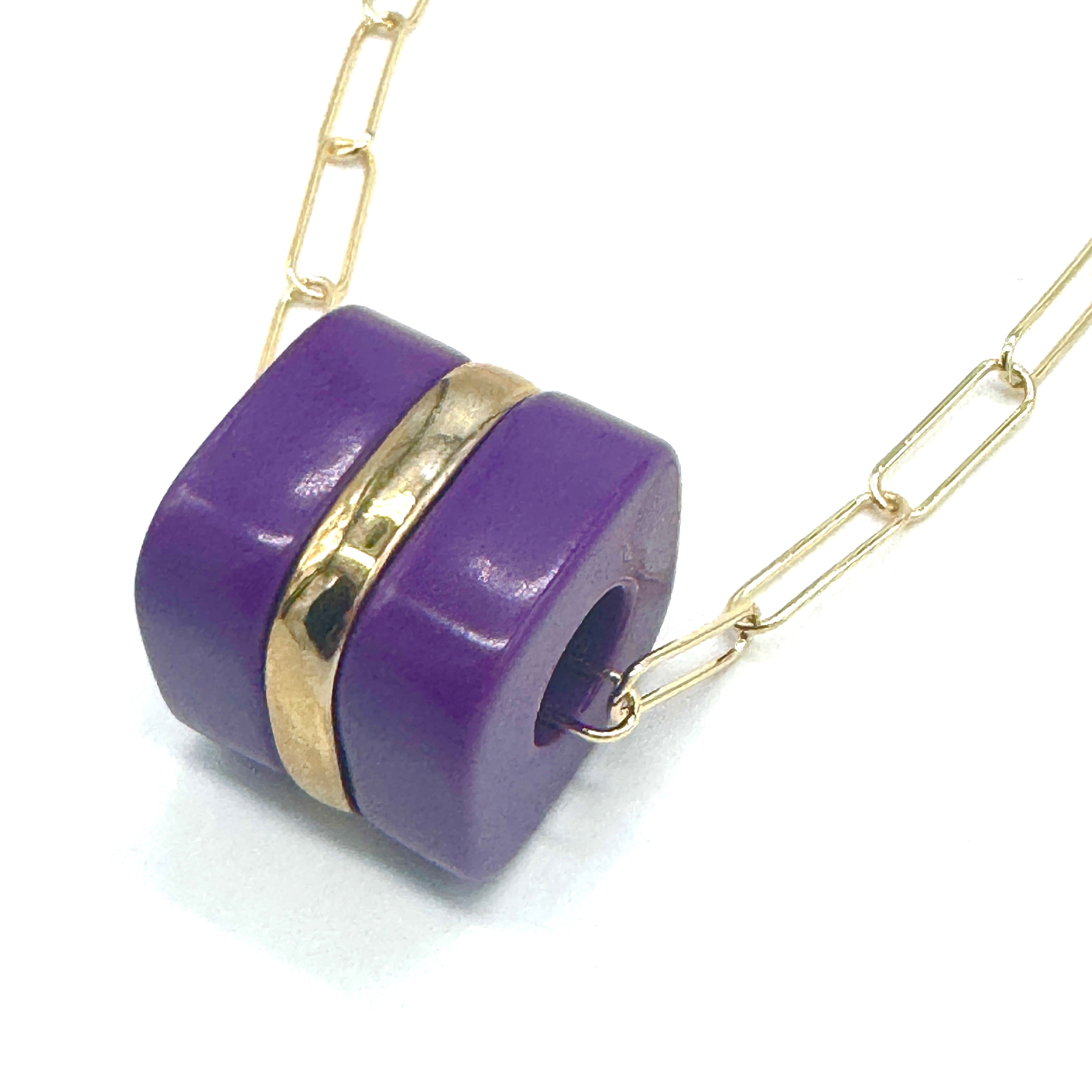 Purple cylindrical pendant with gold accent on a gold chain against a white background
