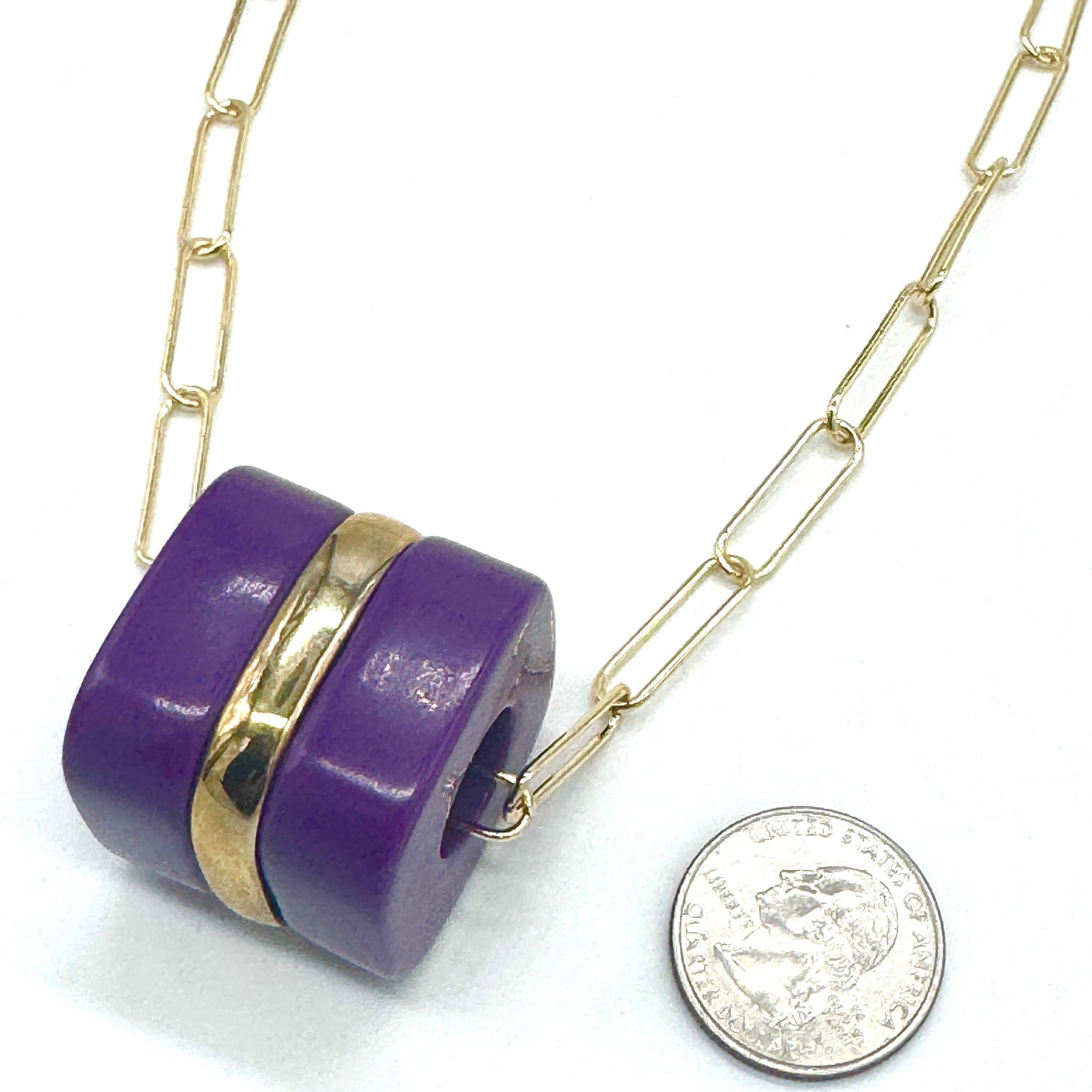 Purple pendant with gold accents on a gold chain, next to a quarter for scale.