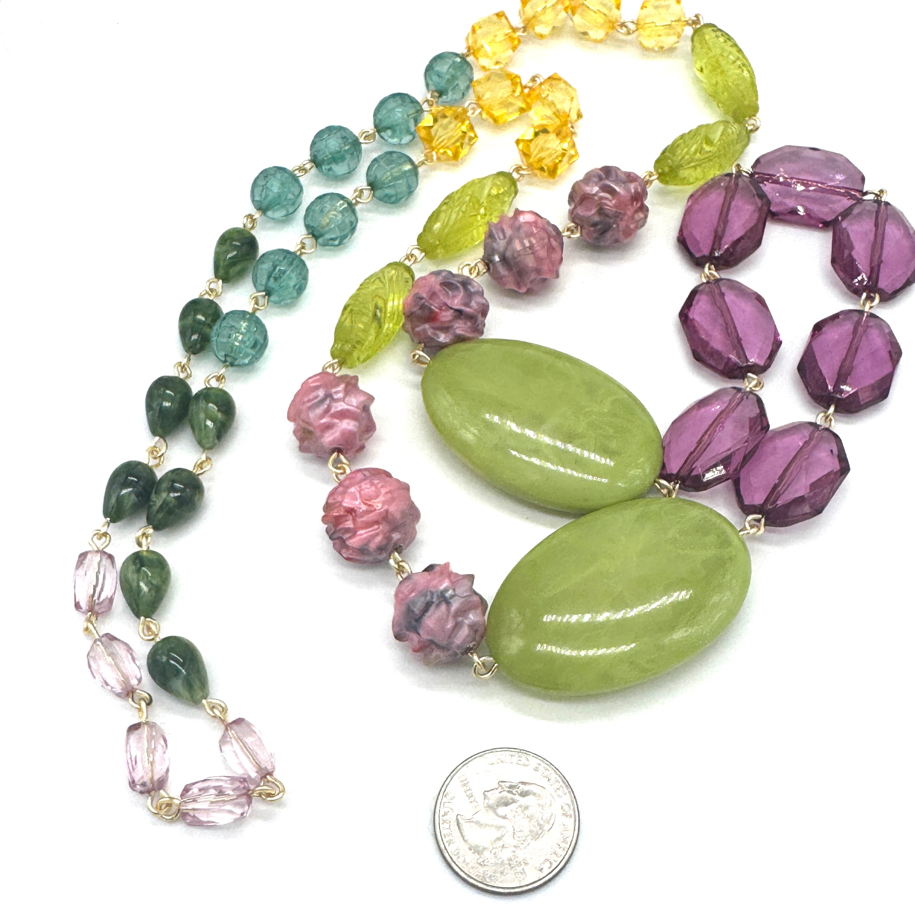 Colorful beaded necklace with large green and purple beads, displayed with a coin for scale.