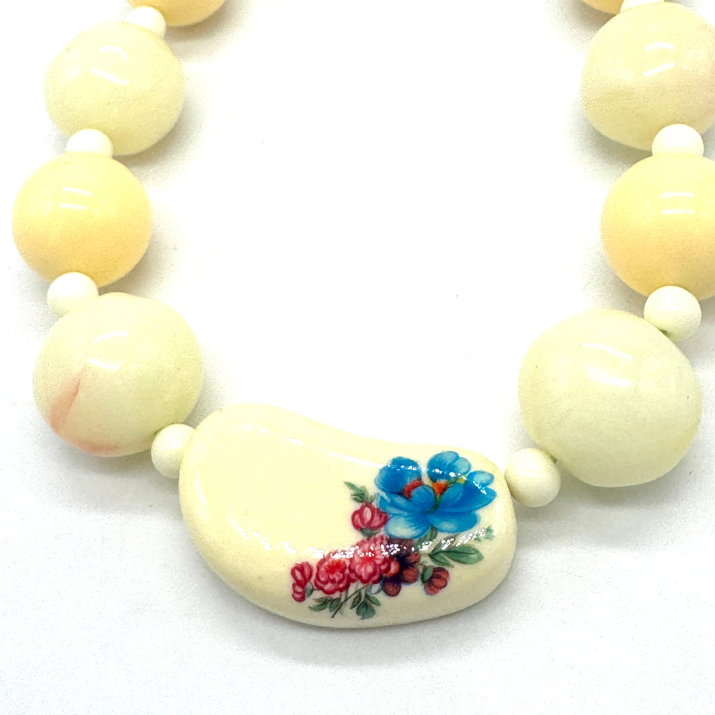 Necklace with cream-colored beads, one of which has a floral design.