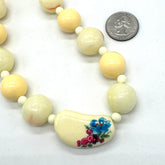 Necklace with large cream-colored beads, one of which has floral design, on a white background.