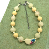 Necklace with white and beige beads, featuring a floral pendant on a green textured surface.
