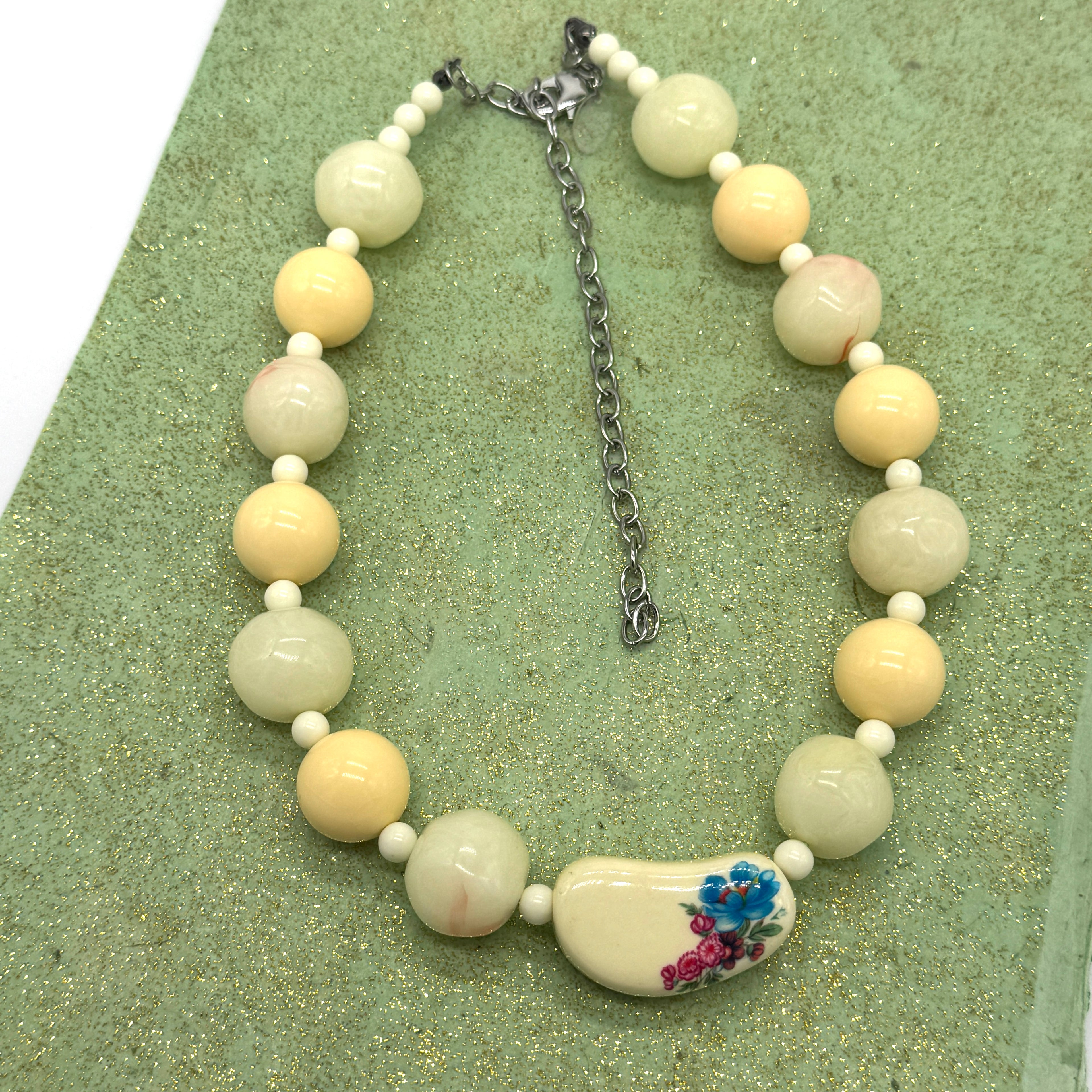 Necklace with white and beige beads, featuring a floral pendant on a green textured surface.