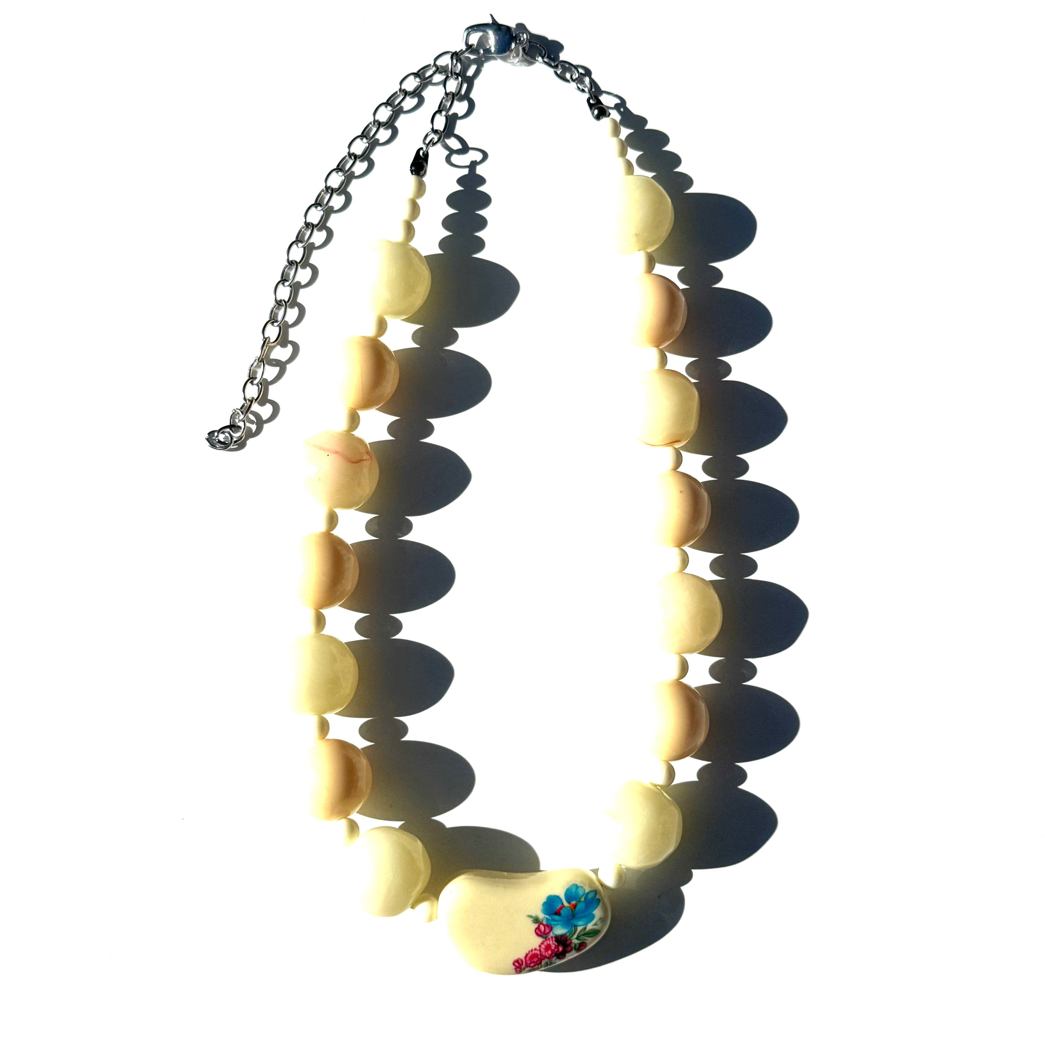 Necklace with yellow beads and a blue flower pendant on a white background
