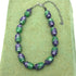 Necklace with green and purple beads on a green textured surface
