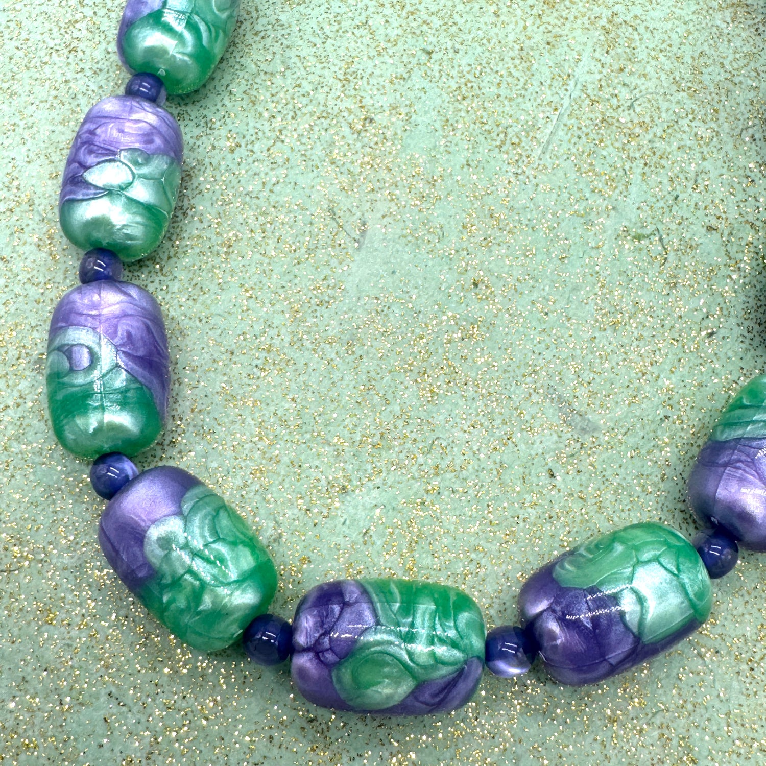 Necklace with green and purple beads on a textured green surface