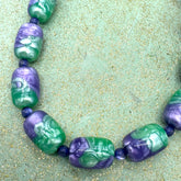 Necklace with green and purple beads on a textured green surface