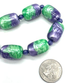 Necklace with green and purple beads next to a quarter for size comparison on a white background