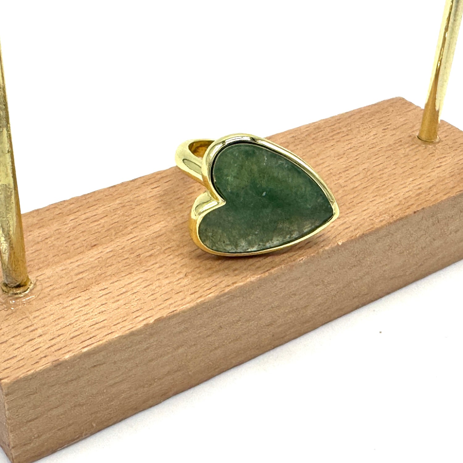 Heart-shaped green stone pendant with gold setting on a wooden stand.