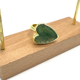Heart-shaped green stone pendant with gold setting on a wooden stand.