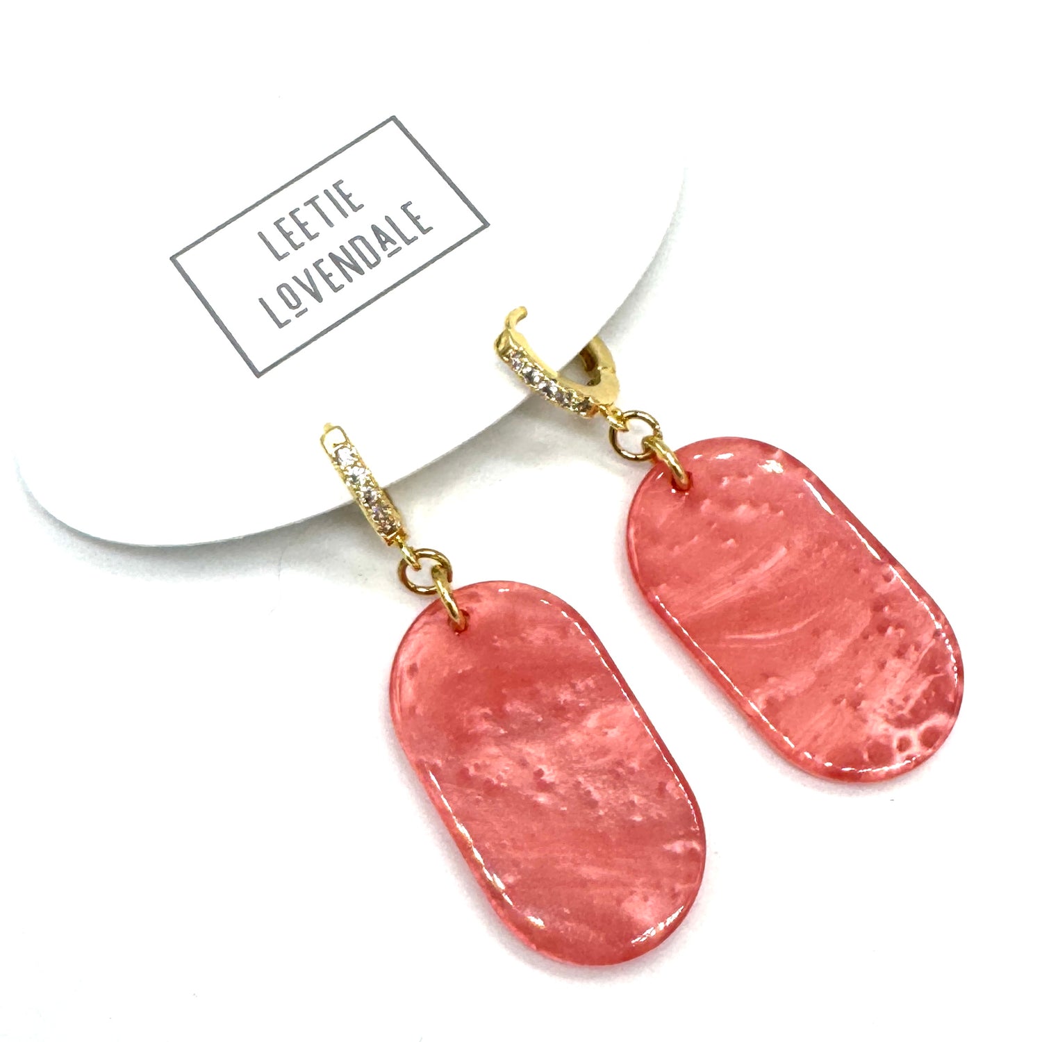 Pink earrings with gold earwires on a white background, featuring the brand &