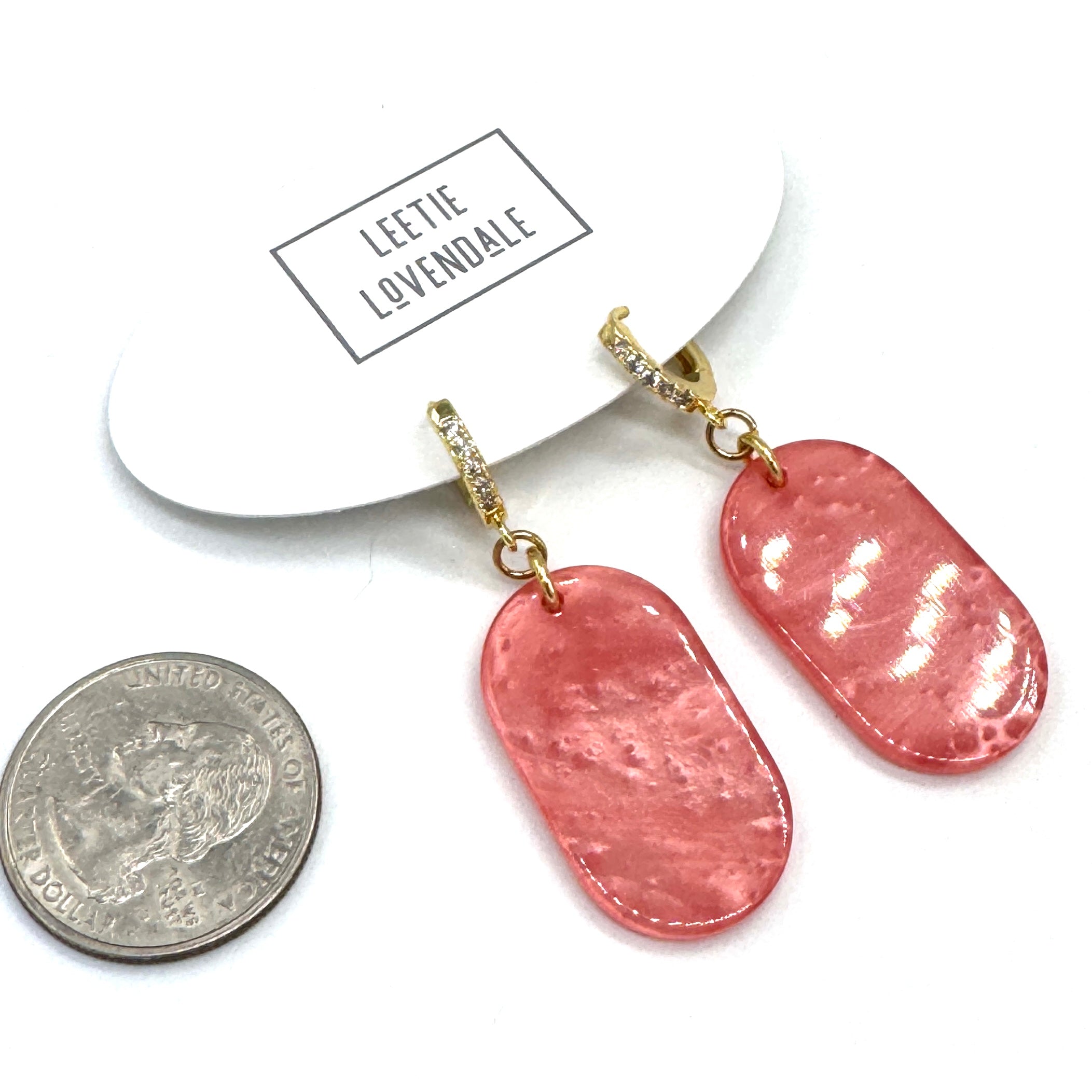 Pink earrings with gold hooks on a white card, next to a coin for scale.