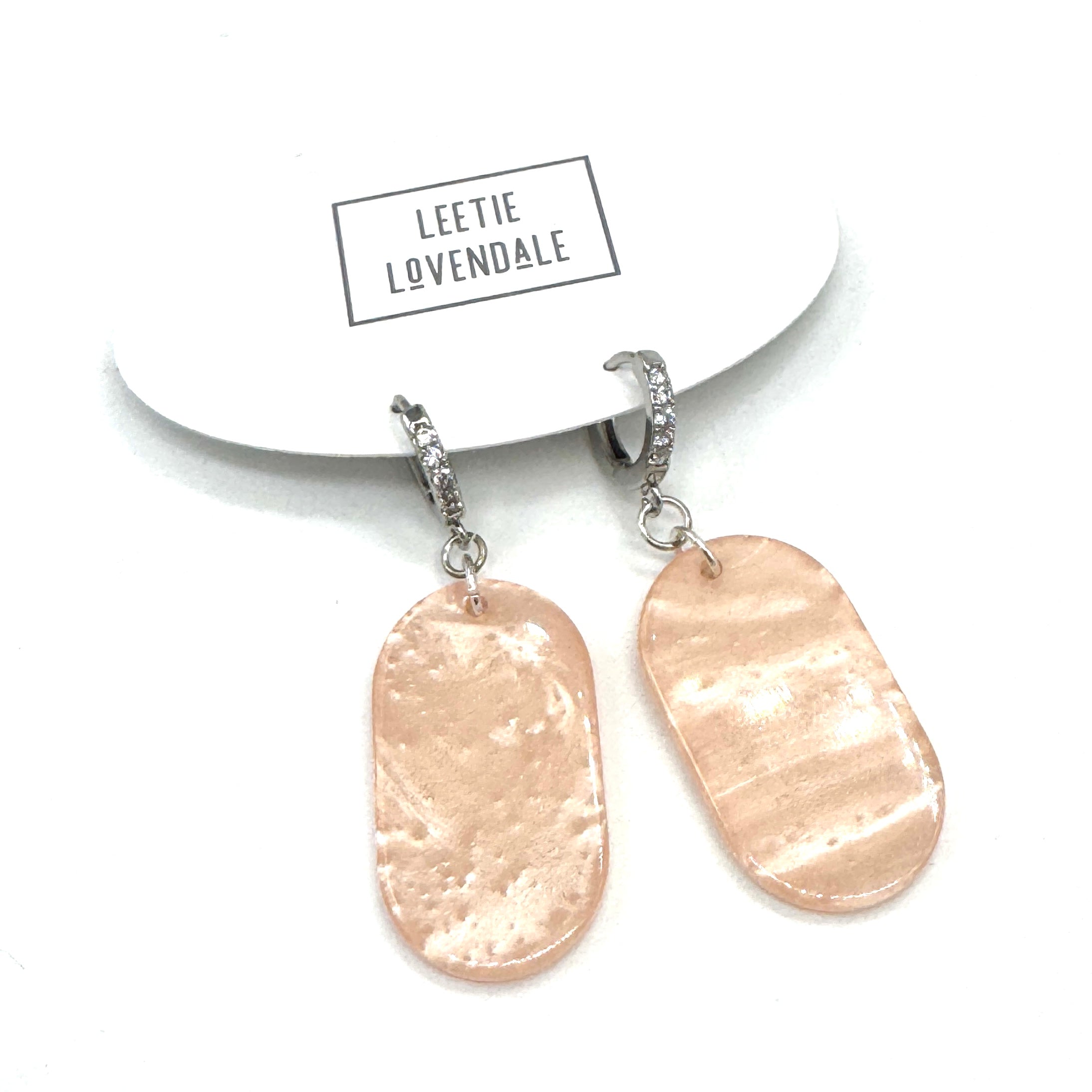 Pair of earrings with pale pink pendants on a white background with &
