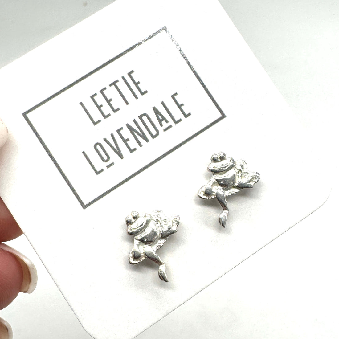 Silver frog-shaped earrings on a card with &