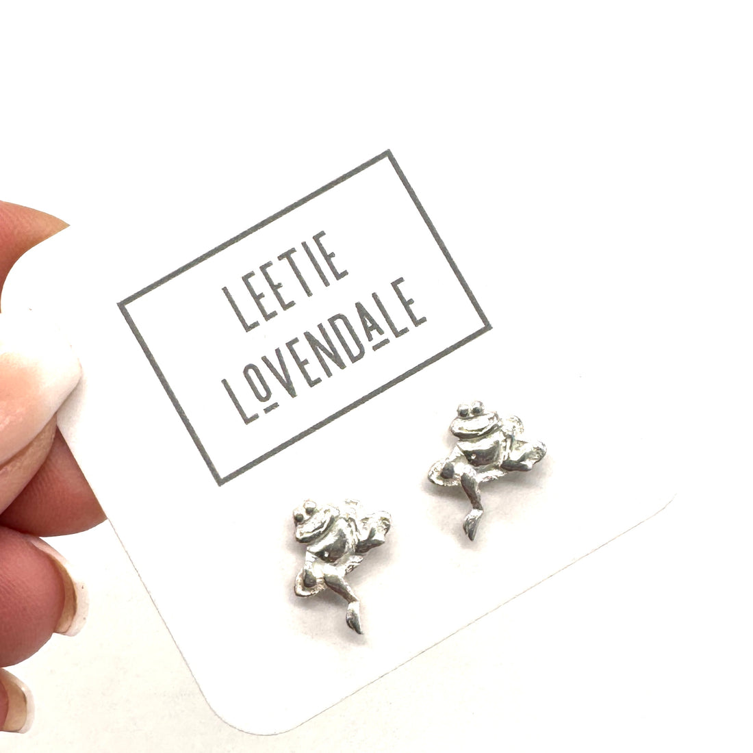 Silver frog-shaped earrings on a card with &