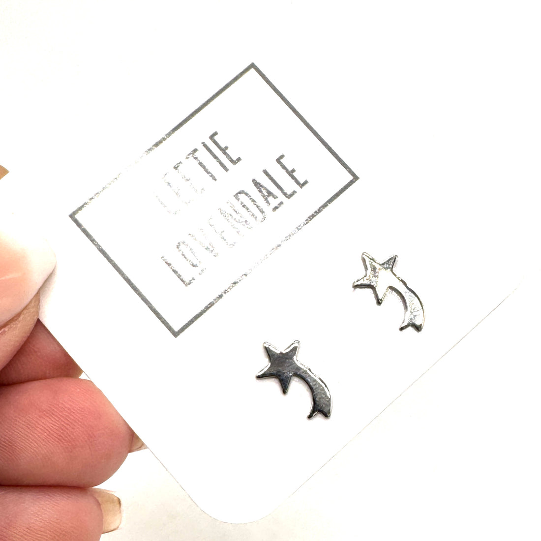 Silver star-shaped earrings on a card held by a hand with a white background