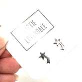 Silver star-shaped earrings on a card held by a hand with a white background