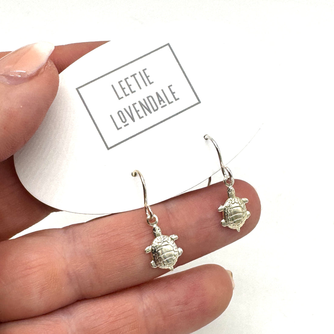 Silver turtle earrings held between fingers with &