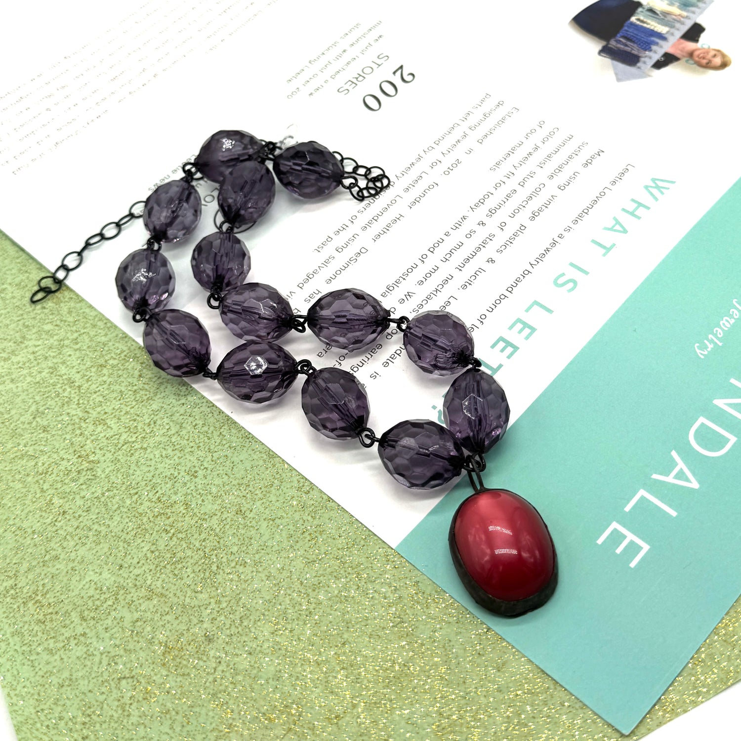 Necklace with purple beads and a red pendant on a magazine background