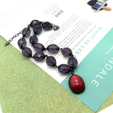 Necklace with purple beads and a red pendant on a magazine background