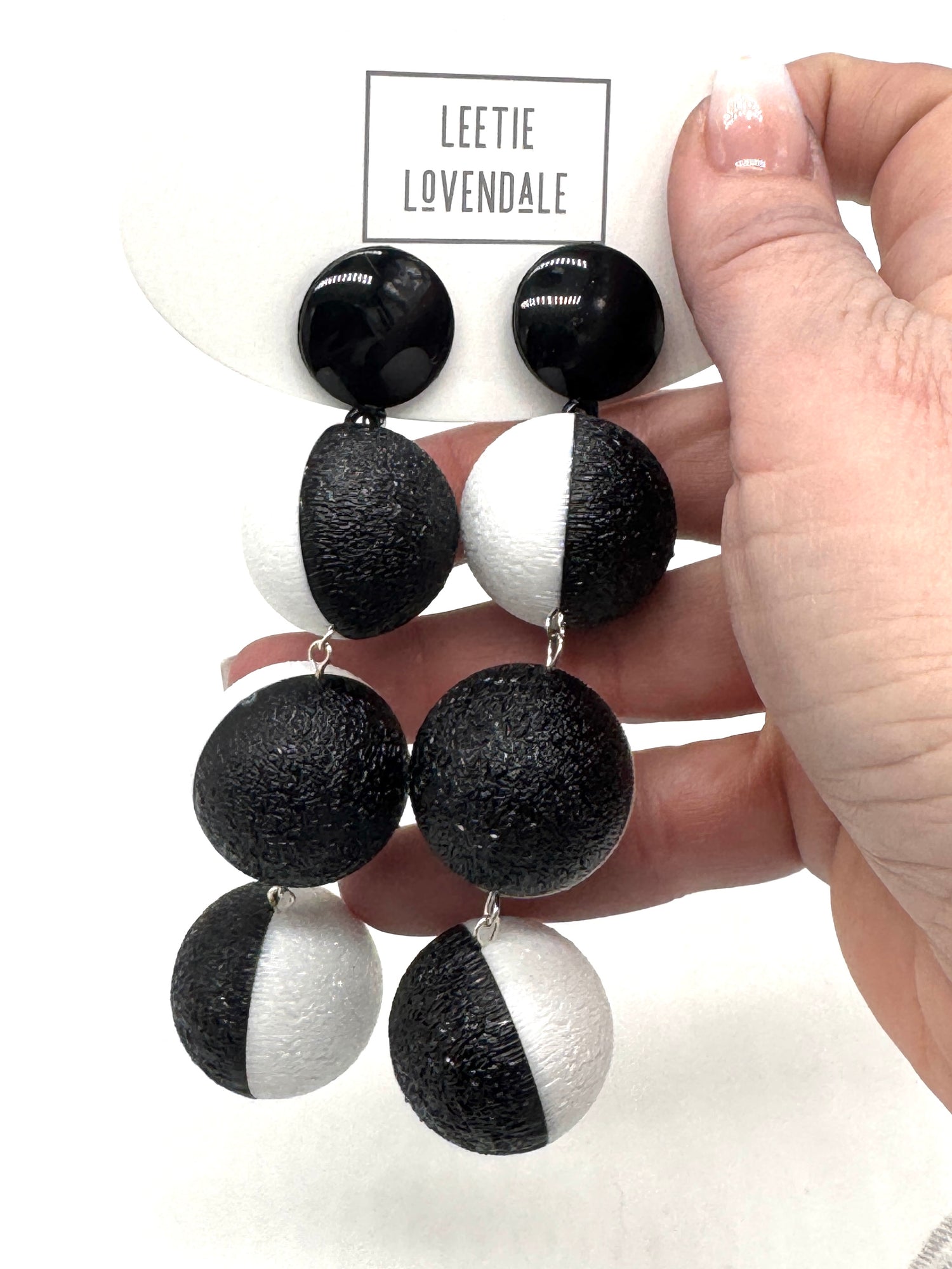 Black and white earrings held by a hand with a brand card in the background