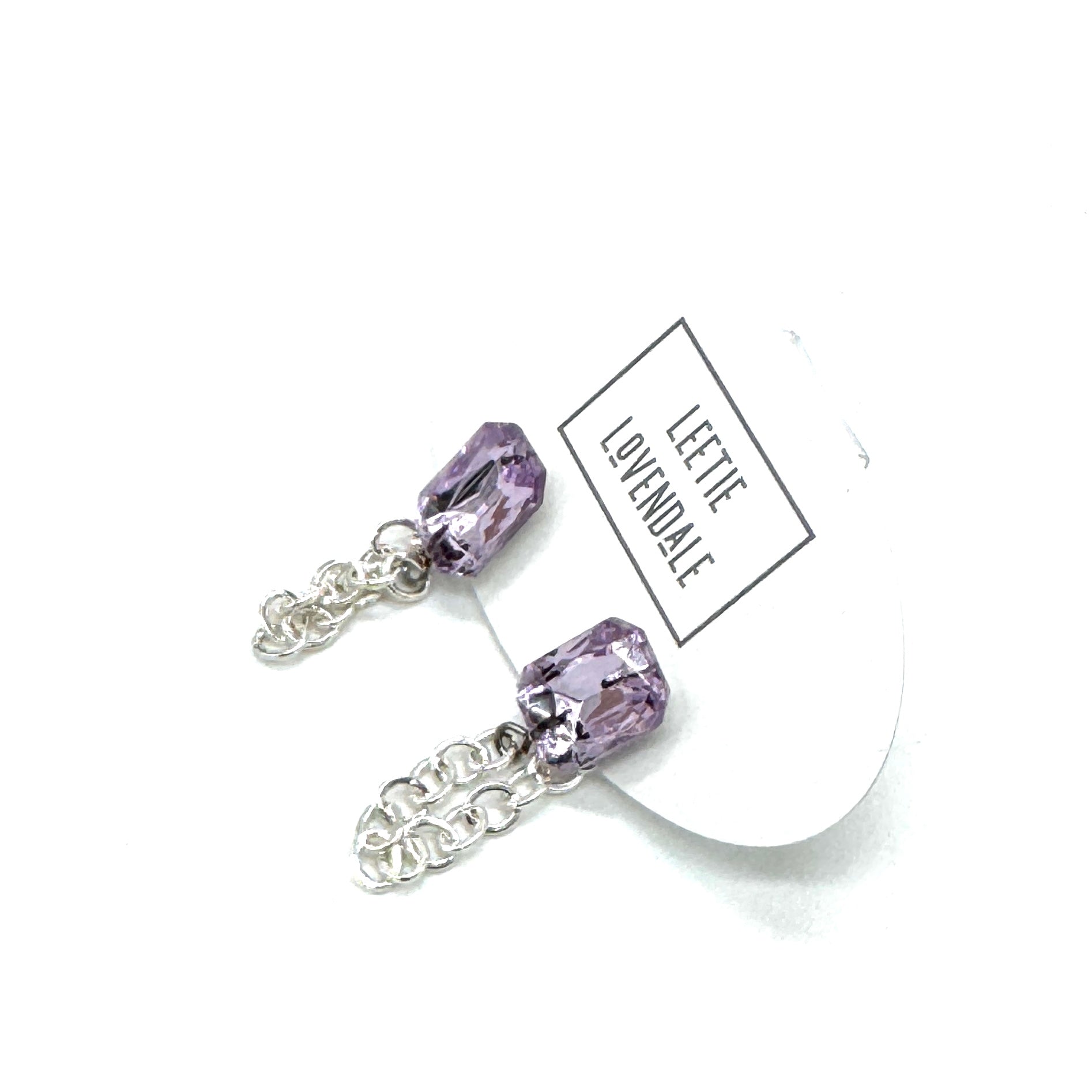 Pair of purple crystal earrings with silver chains on a white background, featuring a &