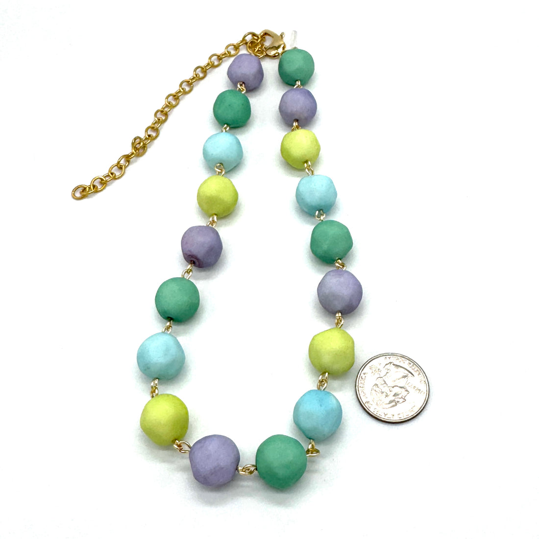 Colorful beaded necklace with a gold chain on a white background, next to a silver coin for scale.