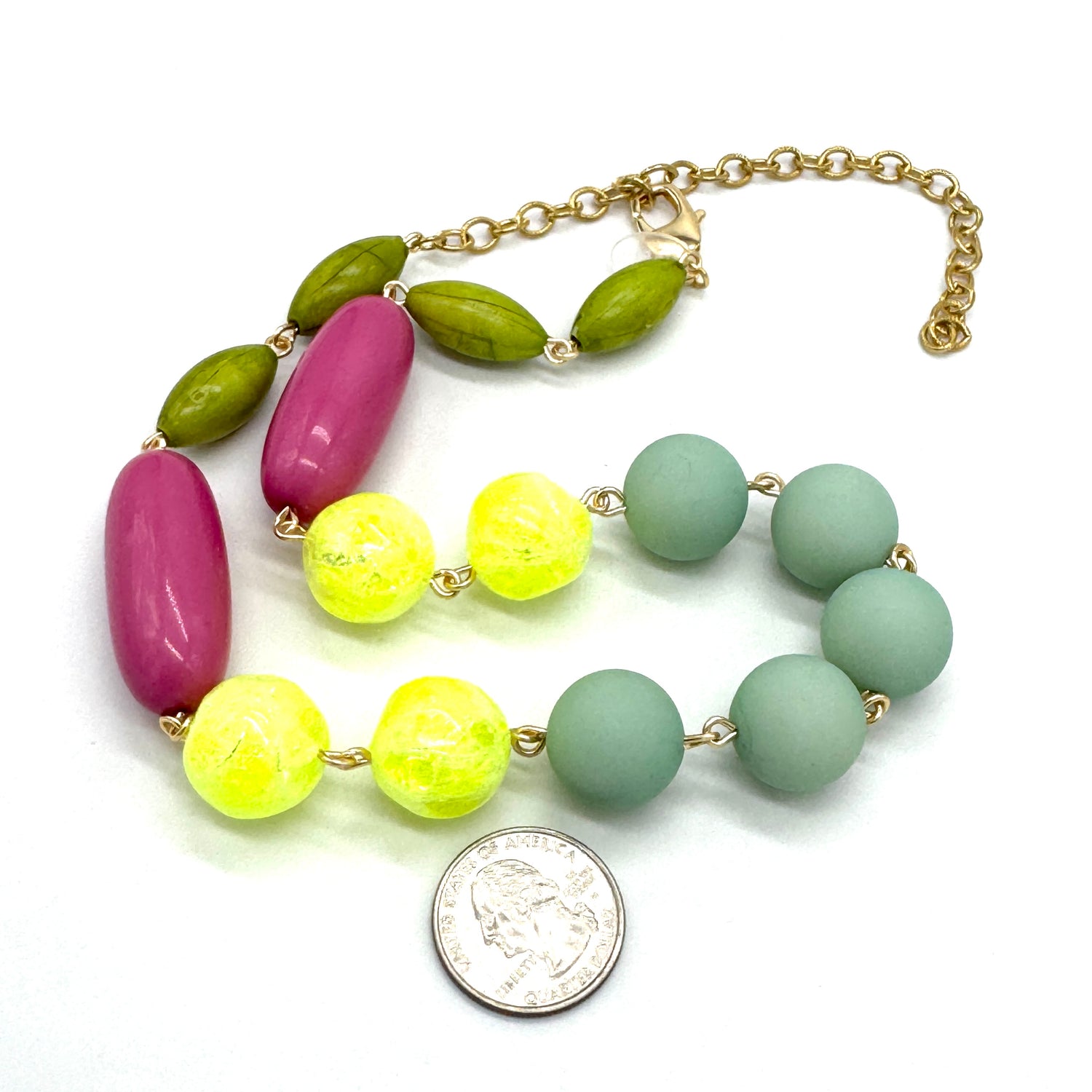 Necklace with colorful beads and a gold chain, next to a quarter for scale on a white background