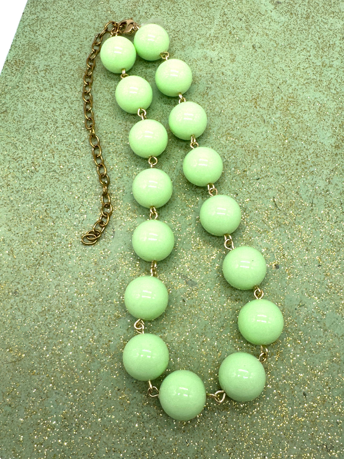 Celadon green beaded necklace on a green glitter background.