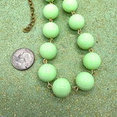 Necklace with green beads and gold chain next to a quarter on a green textured background