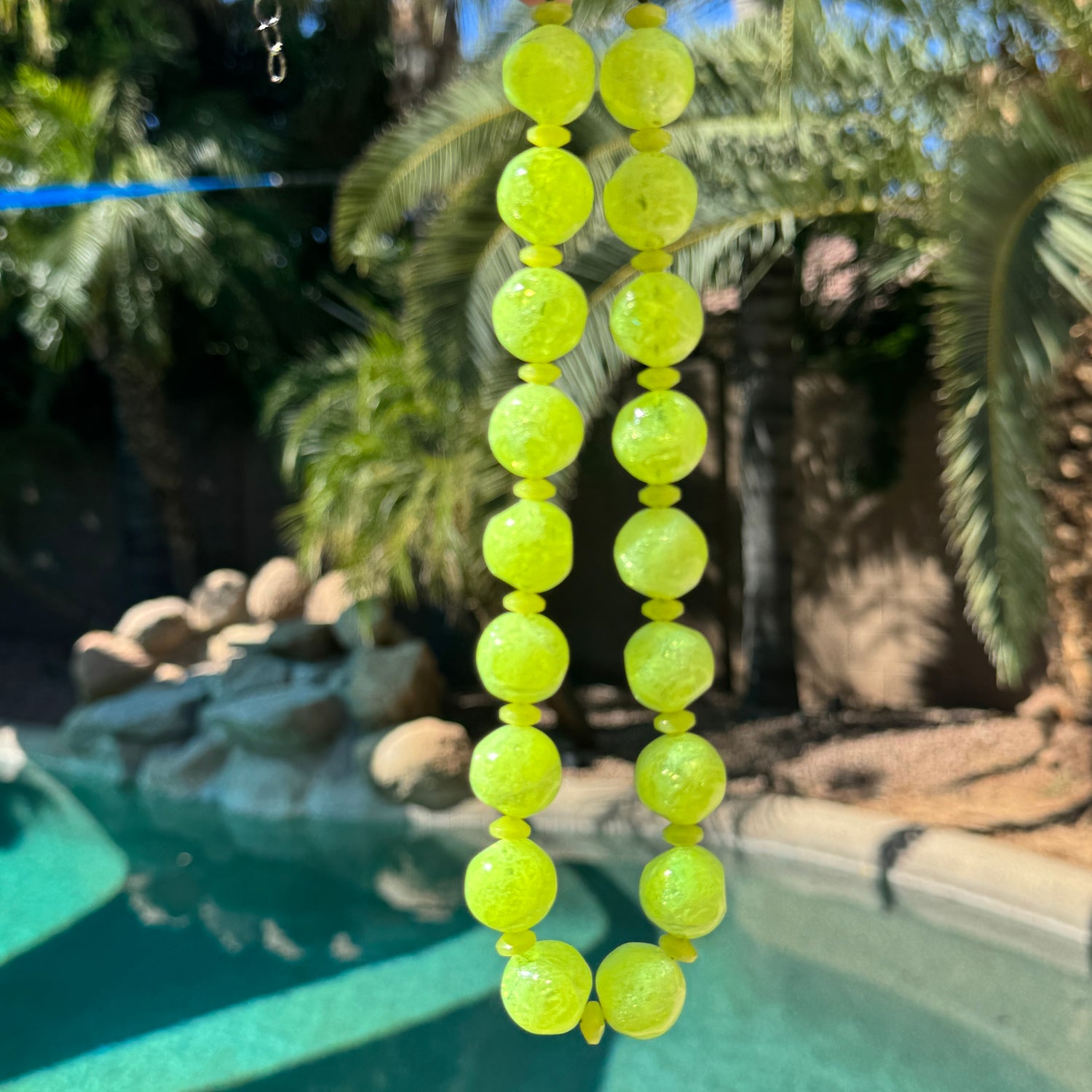 Neon yellow beaded necklace hanging over a pool with palm trees in the background