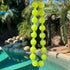 Neon yellow beaded necklace hanging over a pool with palm trees in the background