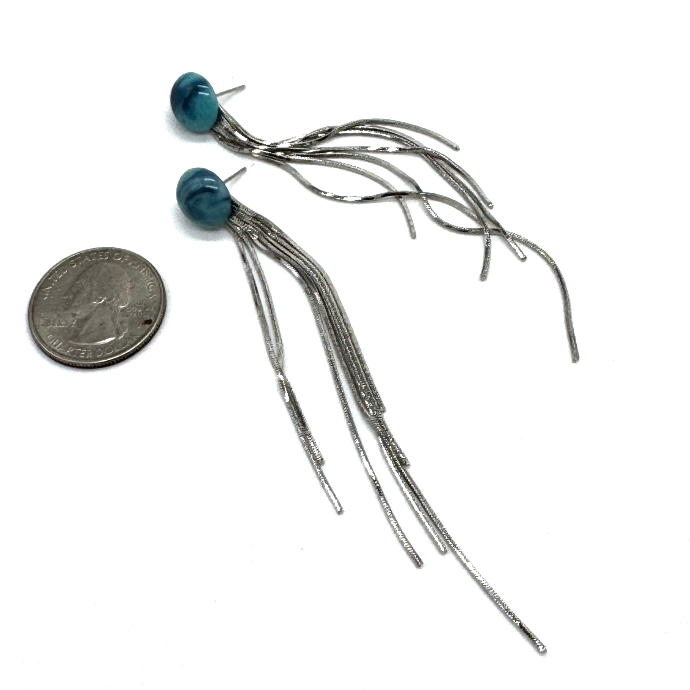 Pair of silver fringe earrings with blue beads next to a quarter for scale on a white background