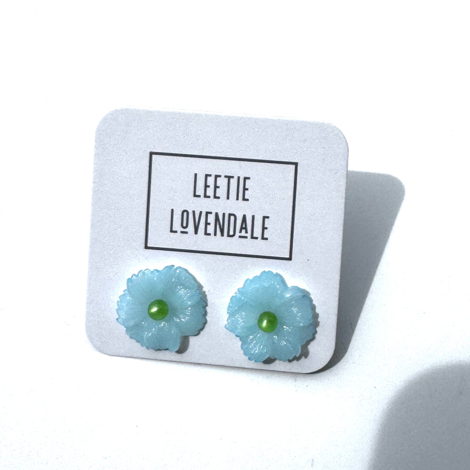 Light blue flower-shaped earrings on a white card with &