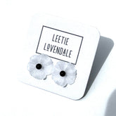 White flower-shaped earrings on a white card with &