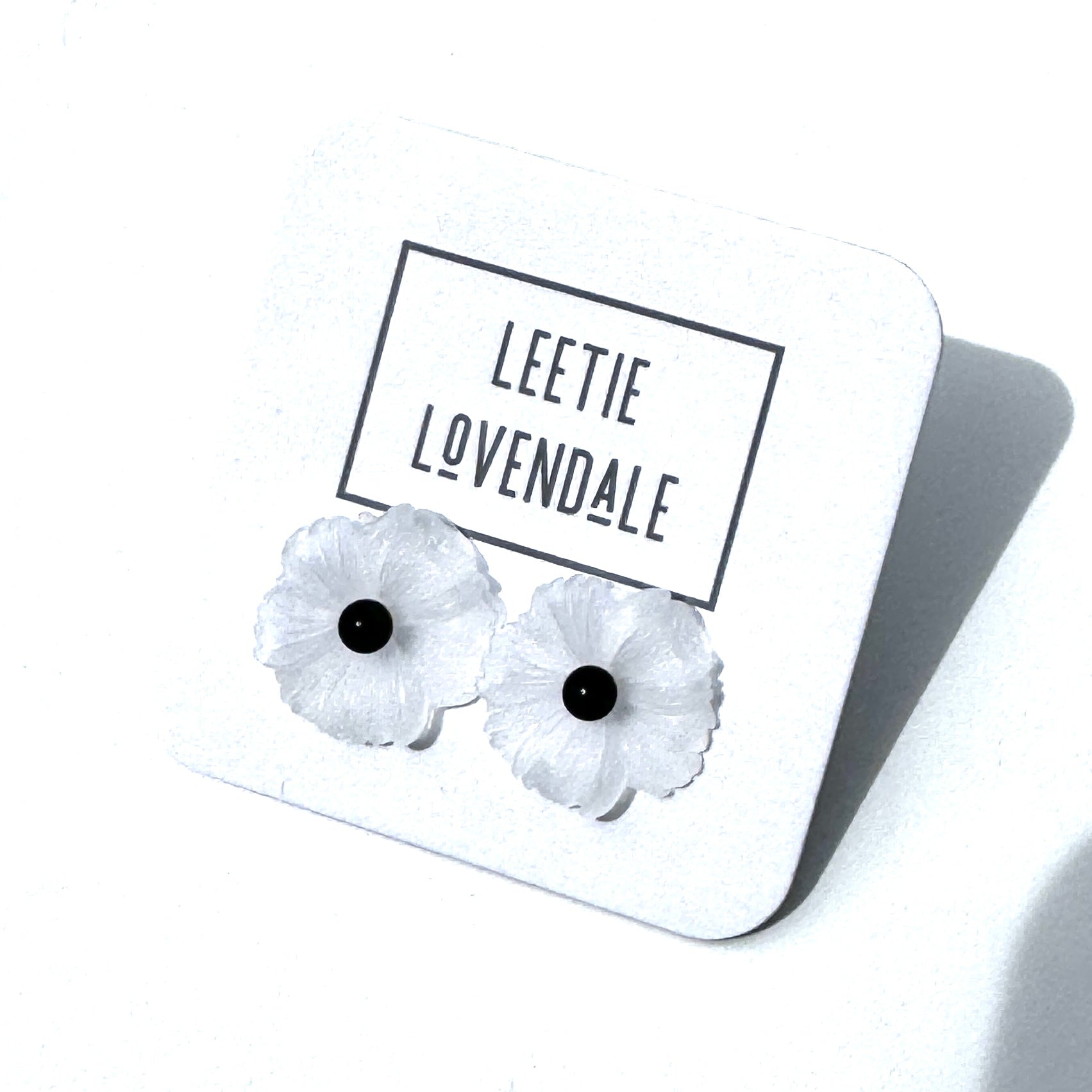 White flower-shaped earrings on a white card with &