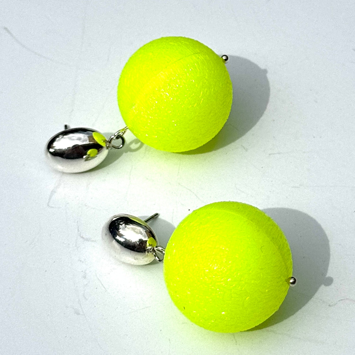 Pair of neon yellow ball earrings with silver posts on a white background