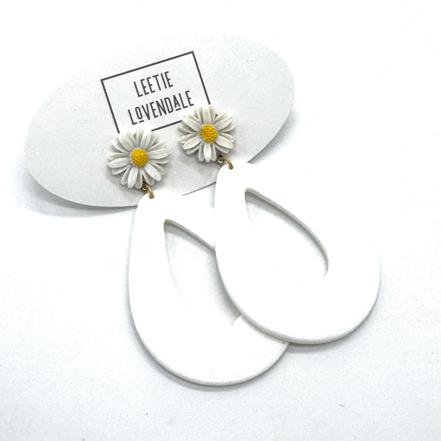 White hoop earrings with daisy flower charms on a white background