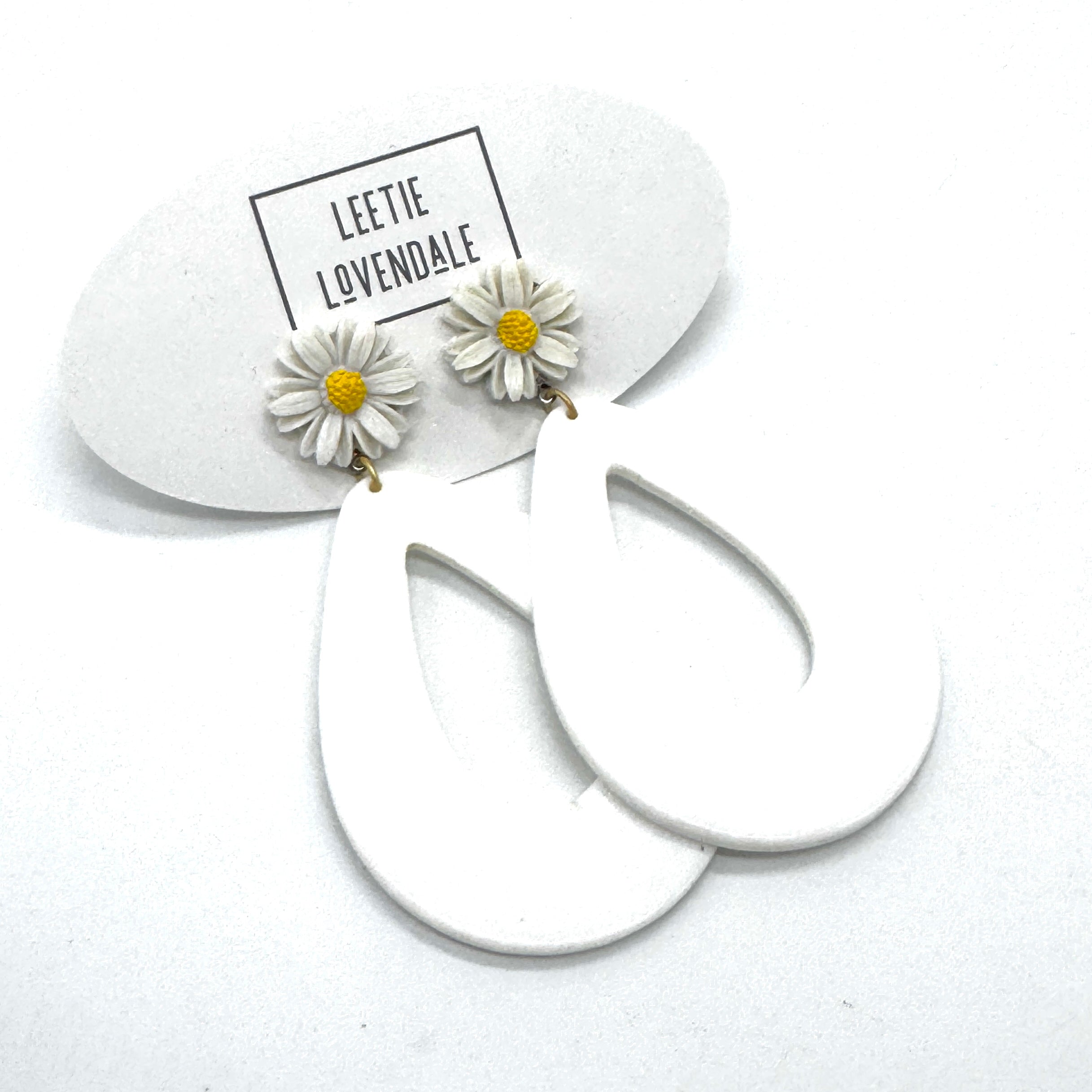 White hoop earrings with daisy flower charms on a white background