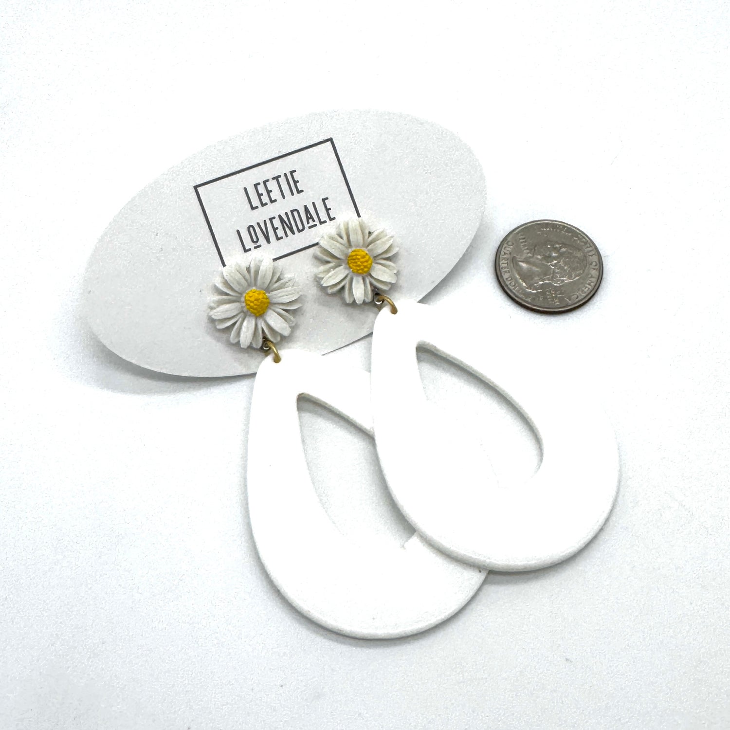 White hoop earrings with daisy flower charms on a white background with &