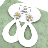 White earrings with floral designs on a green surface, featuring the brand &