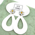White earrings with floral designs on a green surface, featuring the brand &