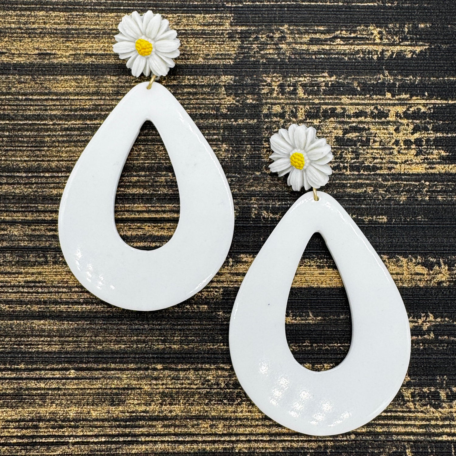 White teardrop earrings with daisy flowers on a textured black and gold background