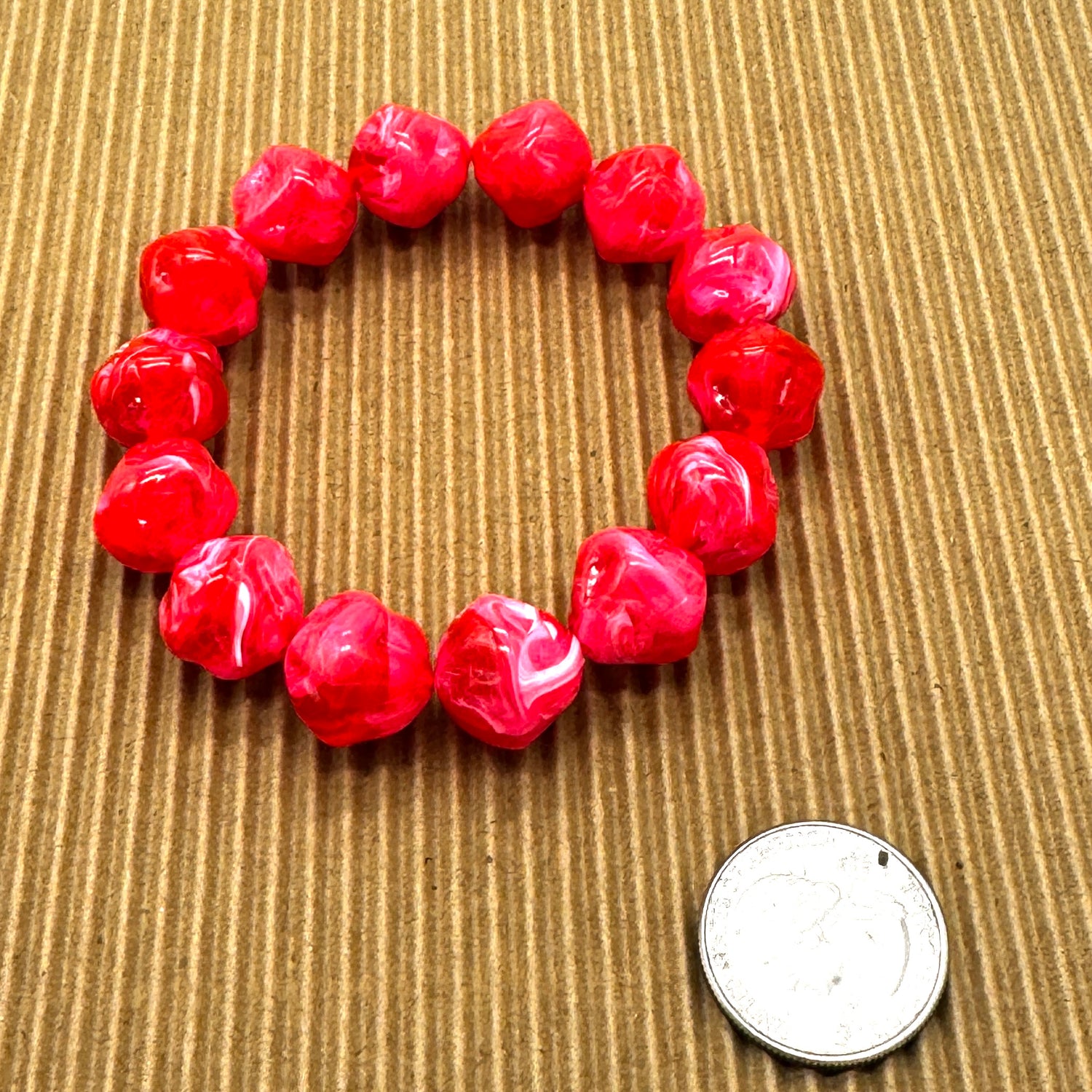 Red beaded bracelet on a textured brown surface with a coin for scale.