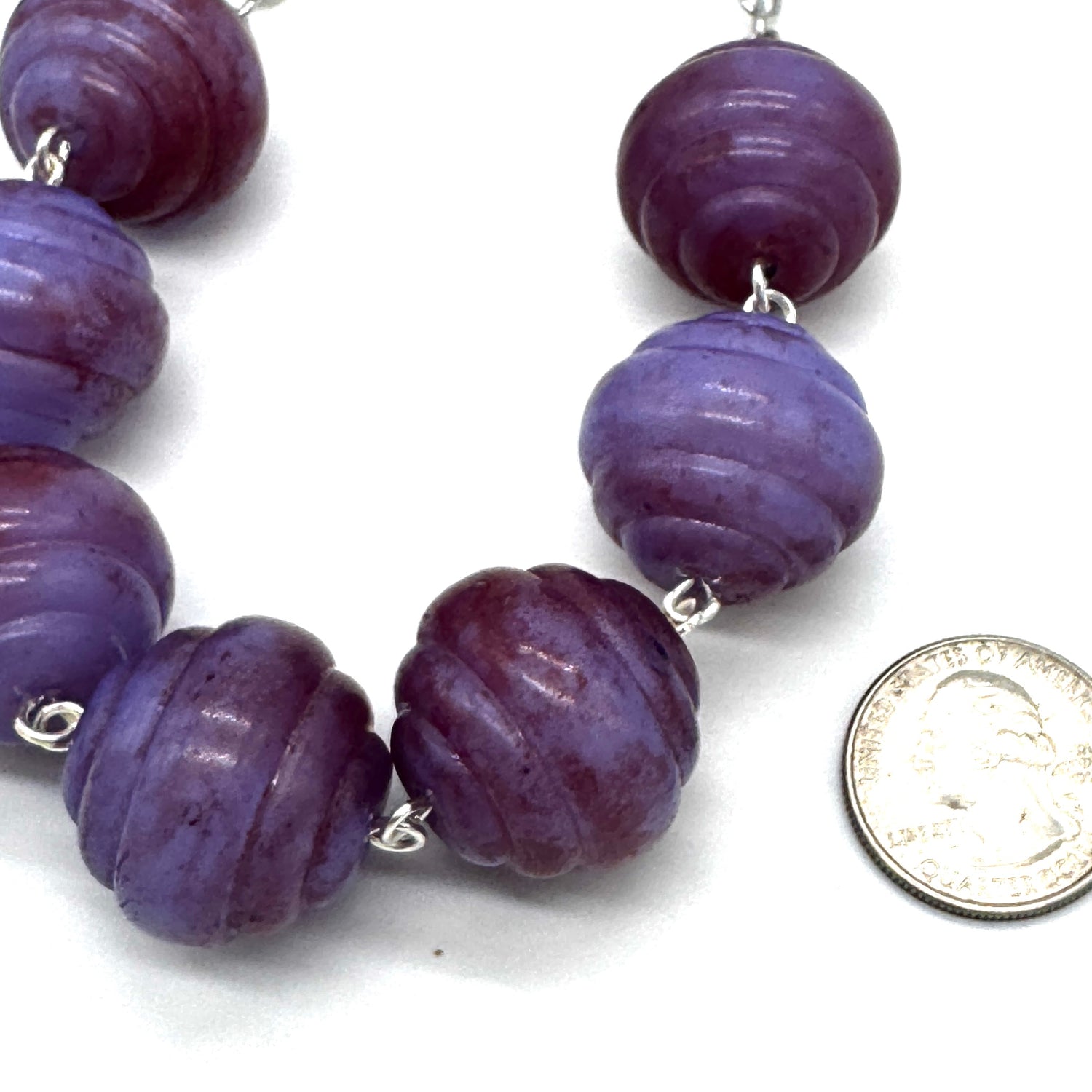 Purple beaded necklace with a coin for scale on a white background