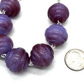 Purple beaded necklace with a coin for scale on a white background